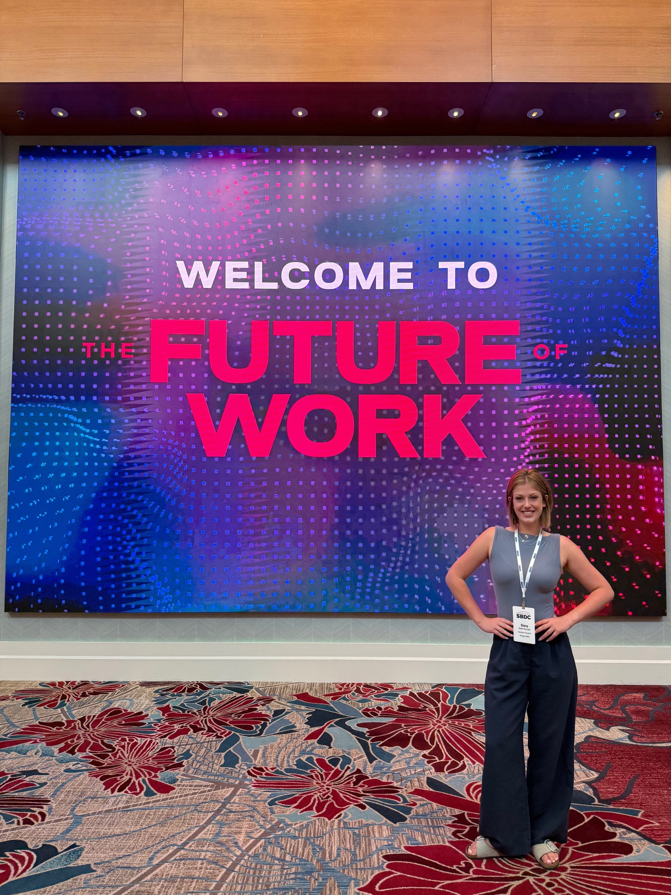 Siera standing beside a conference display reading The Future of Work.